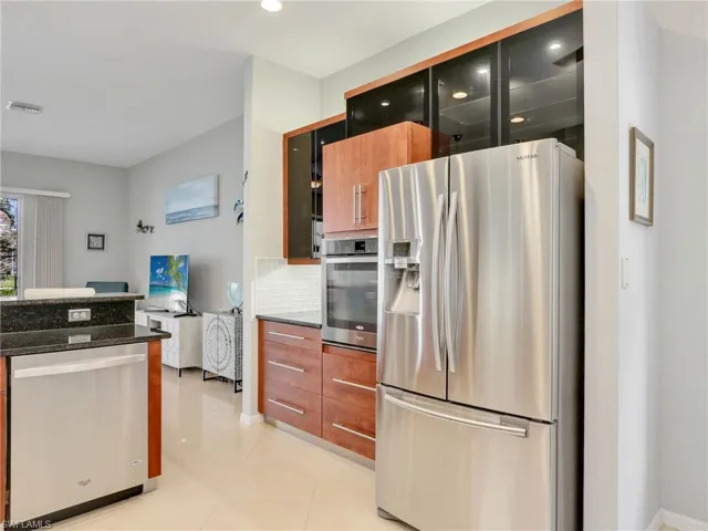 Kitchen with decorative backsplash, stainless steel appliances, light tile patterned flooring, and dark stone countertops