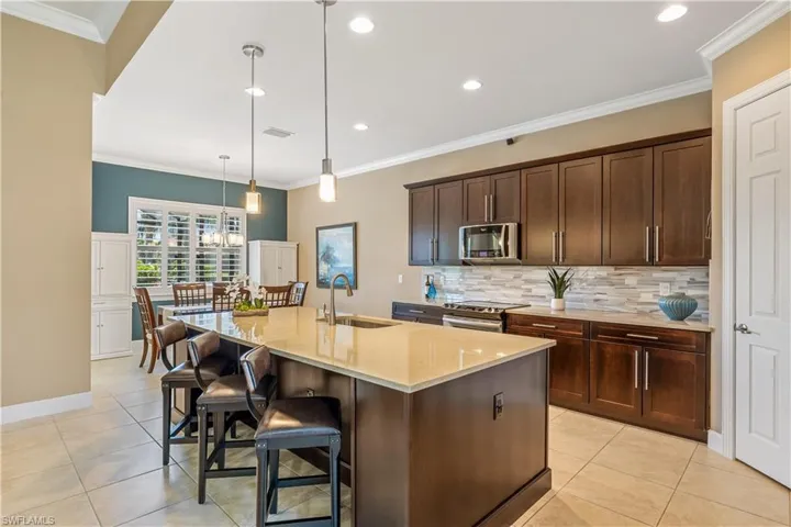 Kitchen with light stone counters, stainless steel appliances, hanging light fixtures, and a large center island with sink