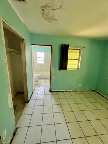 Unfurnished bedroom featuring a textured ceiling, tile patterned flooring, a closet, and ensuite bath