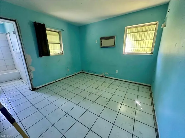 Unfurnished bedroom with multiple windows, tile patterned flooring, and a wall mounted air conditioner