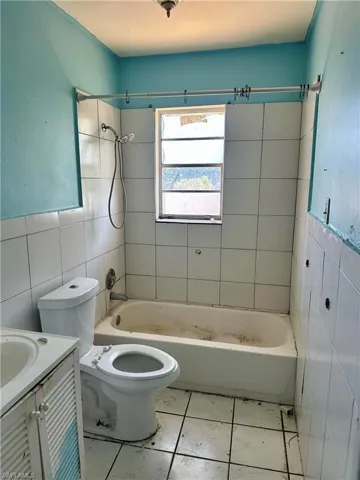 Full bathroom featuring tile walls,  shower combination, vanity, and light tile patterned flooring