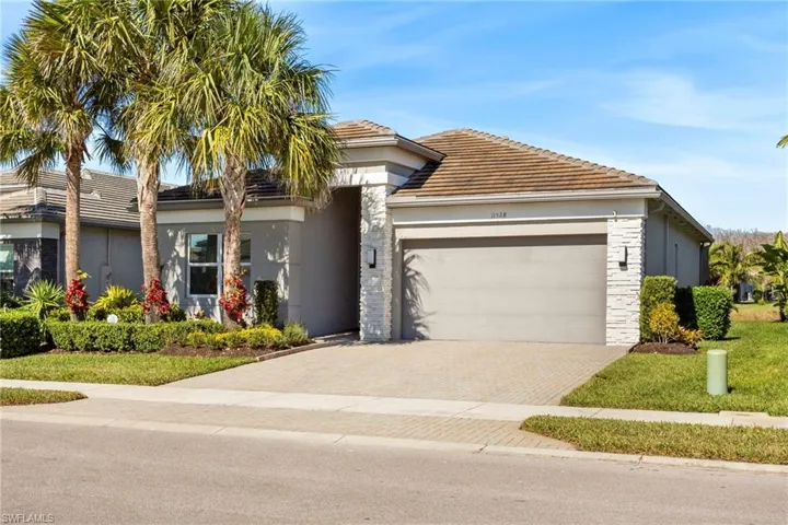 View of front of property with decorative driveway, stucco siding, stone siding, a tile roof, and a garage