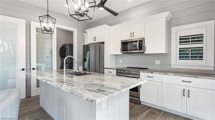 Kitchen, stainless appliances, wood-look flooring, white cabinetry, and a center island with sink