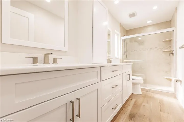 Full bathroom with double vanity, light wood-type flooring, a stall shower, and recessed lighting