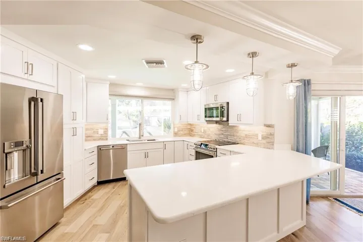 Kitchen with stainless steel appliances, a peninsula, light wood-style flooring, and white cabinetry