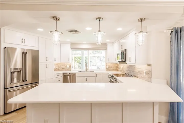 Kitchen featuring a peninsula, stainless steel appliances, white cabinetry, and pendant lighting