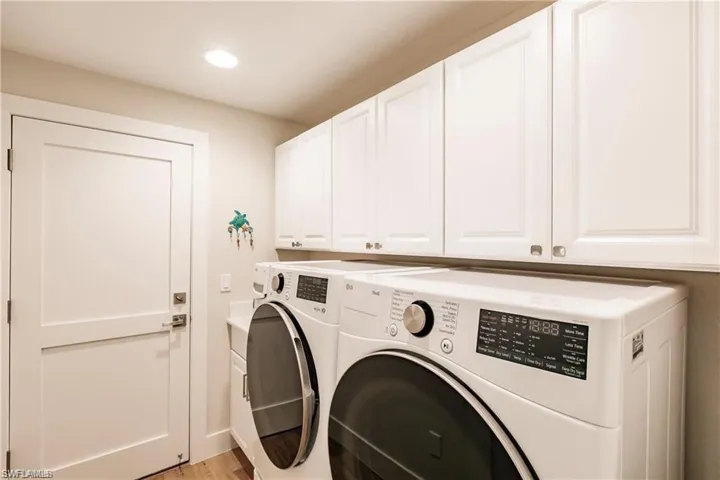 Laundry room with washing machine and clothes dryer, cabinet space, light wood-style flooring, and recessed lighting