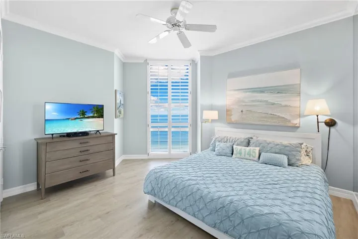 Bedroom with light wood-type flooring, ornamental molding, a ceiling fan, and a wall of windows