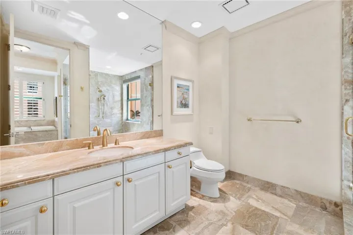 Bathroom featuring vanity, a marble finish shower, crown molding, and recessed lighting