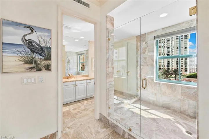 Full bath with vanity, a marble finish shower, recessed lighting, light marble finish floors, and tile walls
