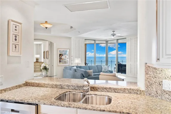 Kitchen with light stone countertops, white cabinets, a water view, a wall of windows, and tasteful backsplash
