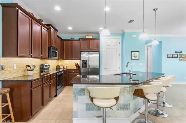 Kitchen with a kitchen breakfast bar, appliances with stainless steel finishes, dark stone counters, tasteful backsplash, and ornamental molding