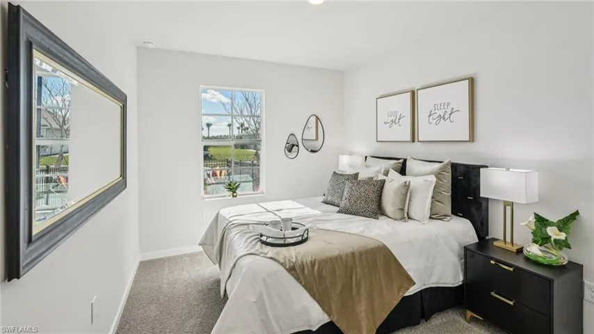 Bright bedroom featuring a large window, plush carpet flooring, and a contemporary wall mirror
