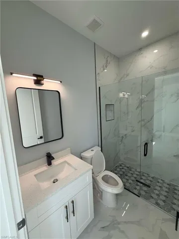 Full bath with light marble finish floors, a marble finish shower, vanity, and recessed lighting