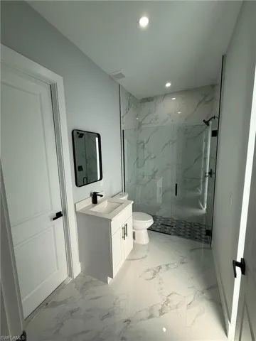 Full bath featuring vanity, a marble finish shower, recessed lighting, and light marble finish floors