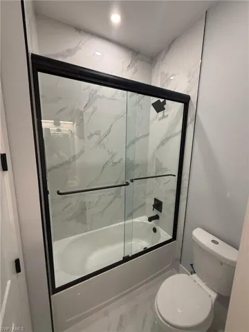 Bathroom with bath / shower combo with glass door and toilet