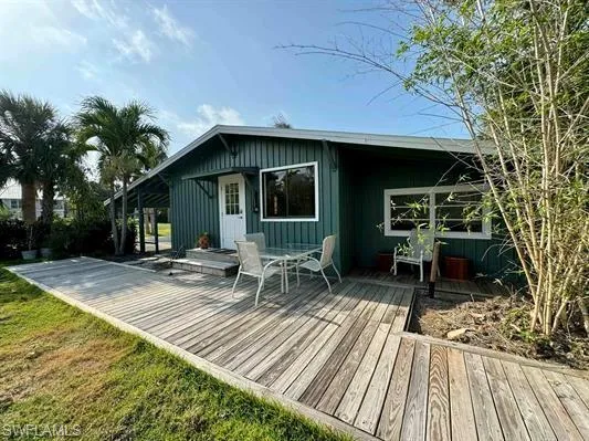 Back of property with a wooden deck, outdoor dining space, a lawn, and board and batten siding