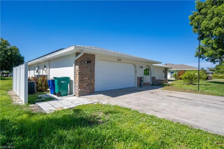 Stucco exterior featuring stone accents, an attached two car garage, a paved driveway, and a white privacy fence.