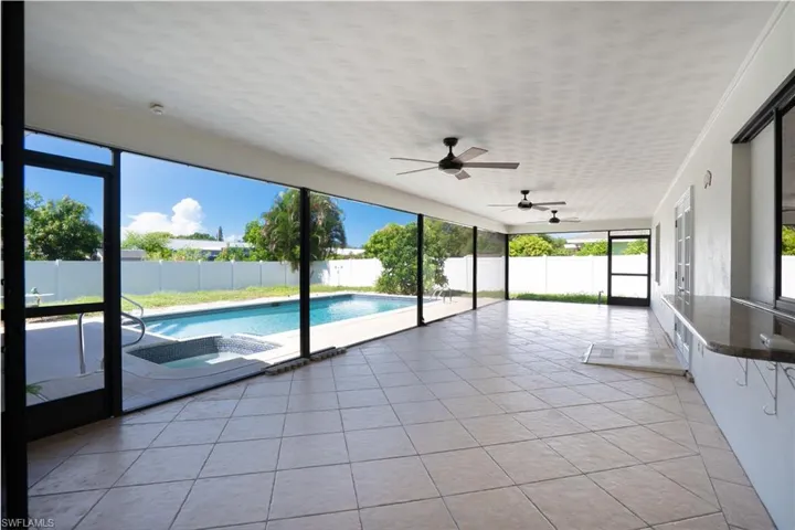 Expansive screened patio featuring a tiled floor, multiple ceiling fans, and a built-in serving bar with a countertop and pass through window