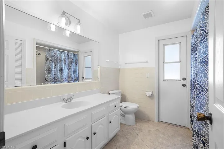 White vanity with an integrated sink, broad wall mirror, vanity fixture, and tiled flooring- bathtub/shower combo- Note the pool door leads out to the lanai for easy access both in and out.