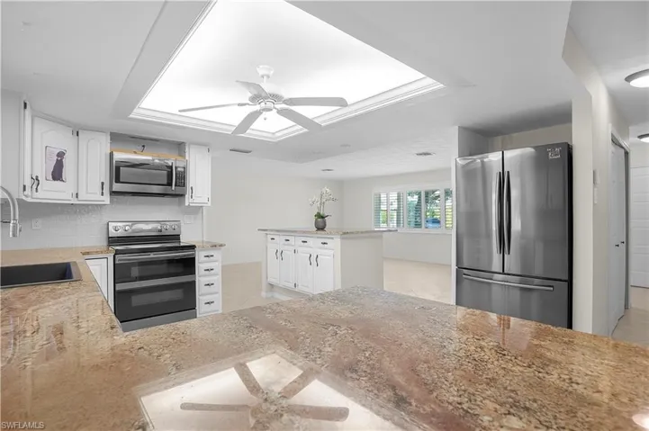 Spacious kitchen featuring extensive counter space, island/breakfast area with a brown-toned granite counters, white cabinetry, stainless steel Samsung appliances, and a central ceiling fan...includes double oven stove/microwave/refrigerator/dishwasher/disposal