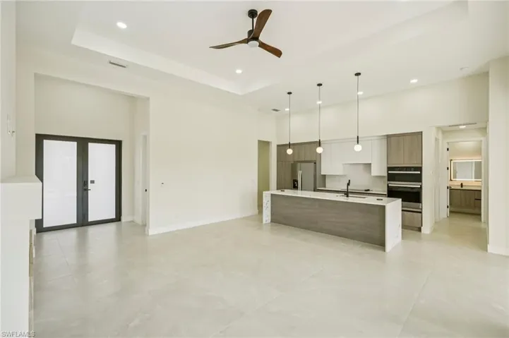 Kitchen with a raised ceiling, modern cabinets, a high ceiling, decorative light fixtures, and an island with sink