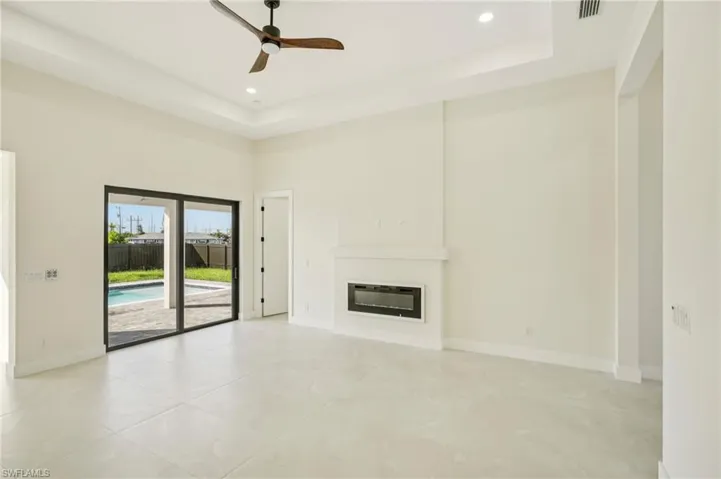 Unfurnished living room featuring a glass covered fireplace, a tray ceiling, a ceiling fan, recessed lighting, and a high ceiling