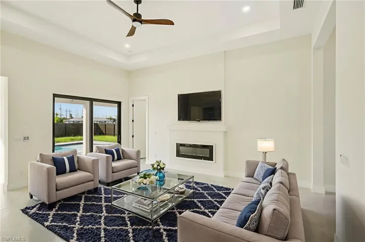 Tiled living room with a glass covered fireplace, a tray ceiling, ceiling fan, and recessed lighting