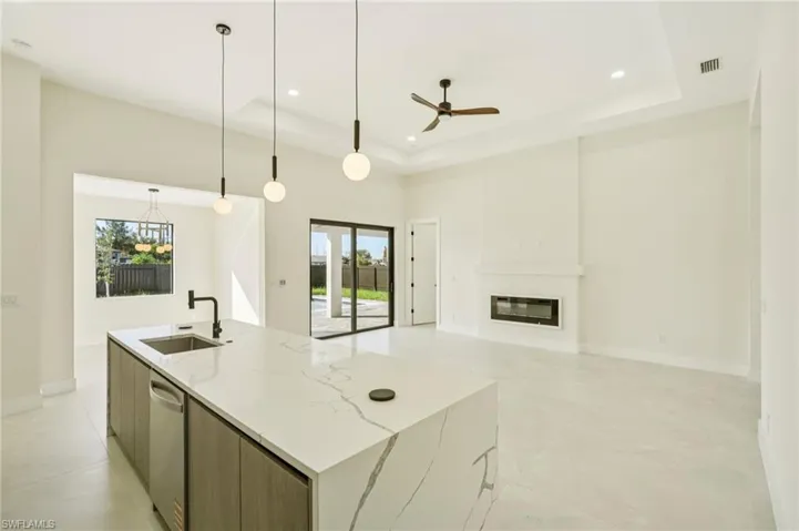 Kitchen with modern cabinets, hanging light fixtures, a glass covered fireplace, light stone counters, and ceiling fan