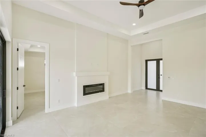 Unfurnished living room featuring a glass covered fireplace, a tray ceiling, recessed lighting, and ceiling fan