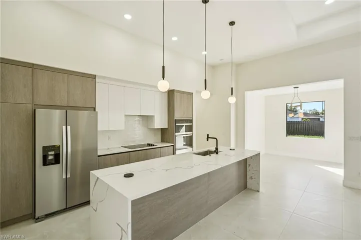 Kitchen with appliances with stainless steel finishes, backsplash, light stone counters, pendant lighting, and modern cabinets