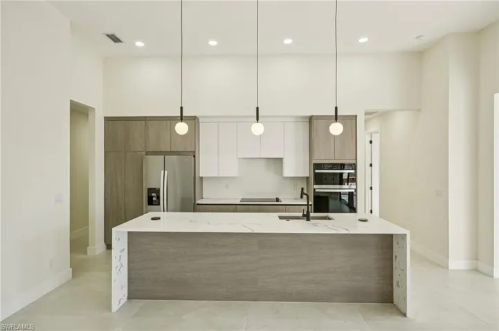 Kitchen featuring light stone countertops, decorative light fixtures, black appliances, white cabinets, and a high ceiling