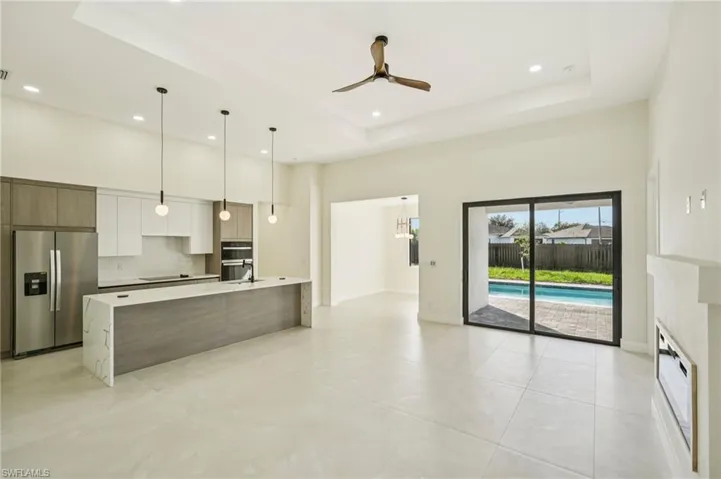 Kitchen featuring a raised ceiling, appliances with stainless steel finishes, white cabinets, pendant lighting, and a ceiling fan