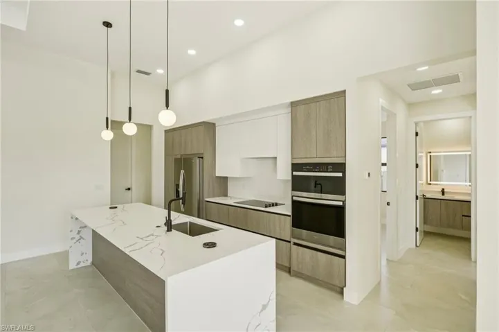Kitchen featuring modern cabinets, pendant lighting, appliances with stainless steel finishes, a kitchen island with sink, and light stone countertops