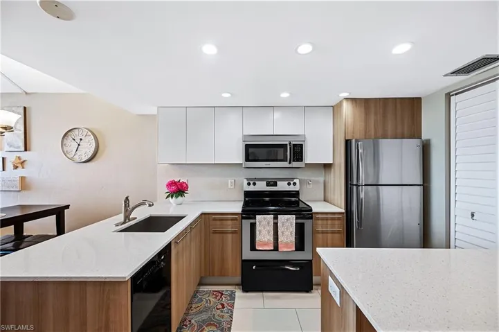 Kitchen featuring white and wood cabinetry, stainless steel appliances, light stone counters, and recessed lighting