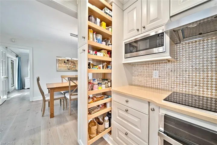 Kitchen with appliances with stainless steel finishes, exhaust hood, decorative backsplash, white cabinets, and light hardwood / wood-style flooring