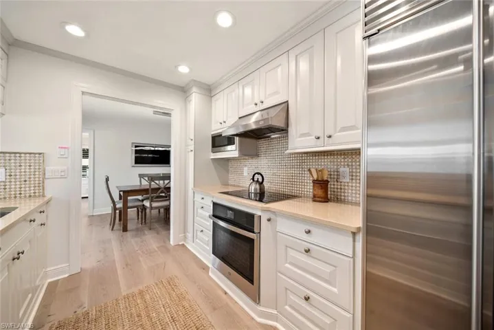 Kitchen featuring built in appliances, white cabinetry, ornamental molding, backsplash, and light hardwood / wood-style flooring
