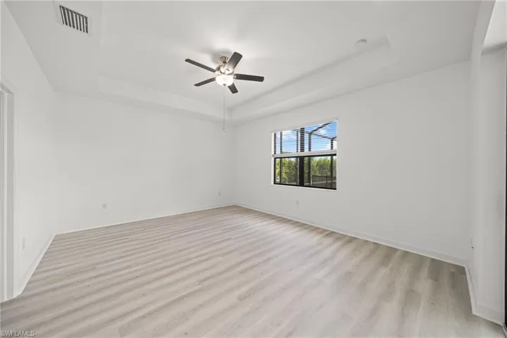 Unfurnished room with a raised ceiling, light wood-style floors, and ceiling fan