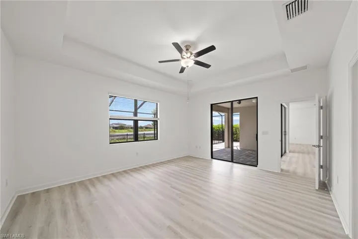 Unfurnished room featuring a tray ceiling, light wood-style flooring, and ceiling fan
