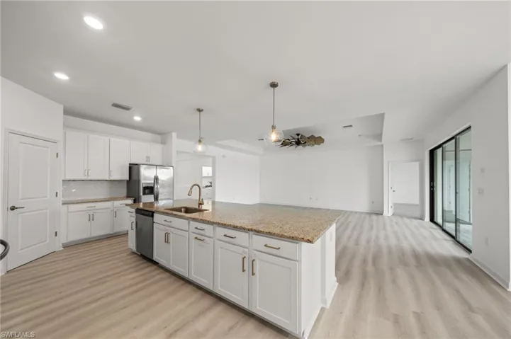 Kitchen featuring light wood finished floors, white cabinets, decorative backsplash, appliances with stainless steel finishes, and hanging light fixtures