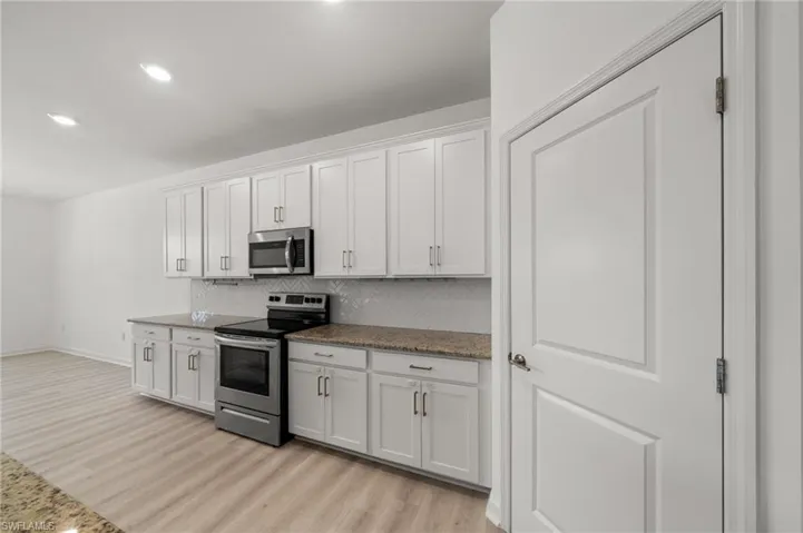 Kitchen featuring stainless steel appliances, light wood finished floors, decorative backsplash, white cabinets, and recessed lighting
