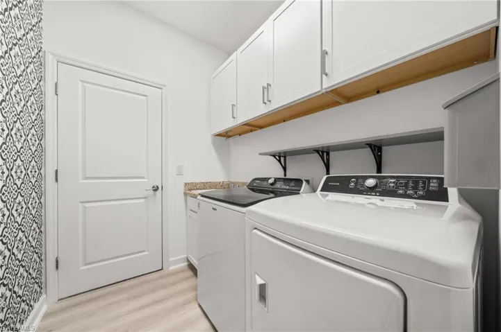 Laundry area with wallpapered walls, light wood finished floors, washer and dryer, and cabinet space