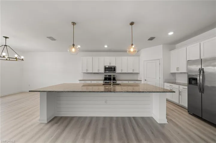 Kitchen featuring stainless steel appliances, light wood finished floors, a kitchen island with sink, decorative backsplash, and white cabinets