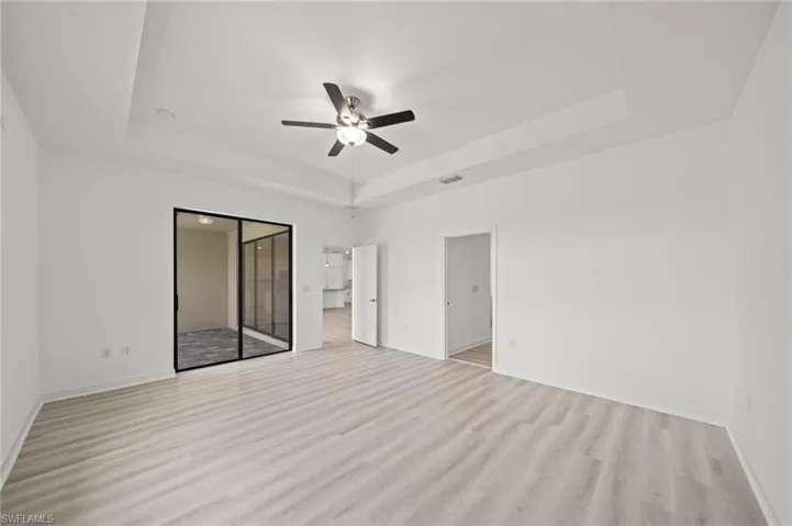 Unfurnished bedroom with a raised ceiling, light wood-style floors, a ceiling fan, and a closet