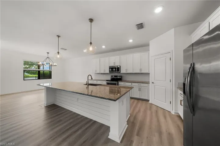 Kitchen featuring appliances with stainless steel finishes, light wood finished floors, a center island with sink, white cabinets, and backsplash