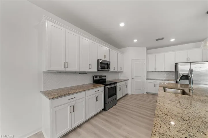 Kitchen featuring stainless steel appliances, decorative backsplash, white cabinets, light stone countertops, and light wood finished floors