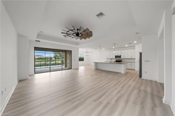 Unfurnished living room featuring a raised ceiling, light wood finished floors, recessed lighting, a ceiling fan, and a chandelier