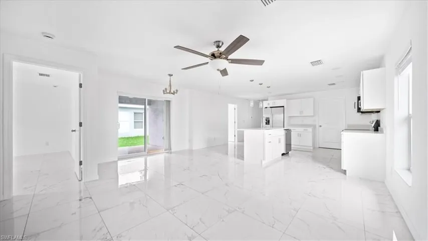 Unfurnished living room featuring light marble finish flooring, plenty of natural light, ceiling fan, and a chandelier