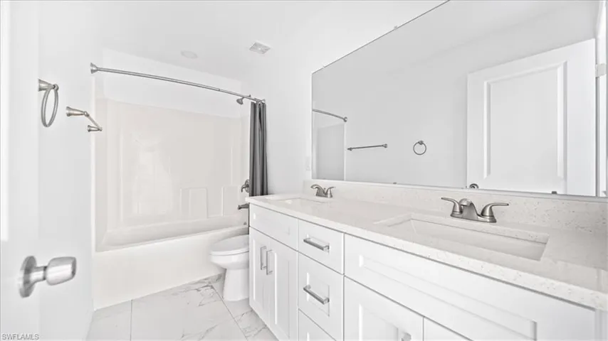 Full bathroom with shower / bathtub combination with curtain, double vanity, and light marble finish floors