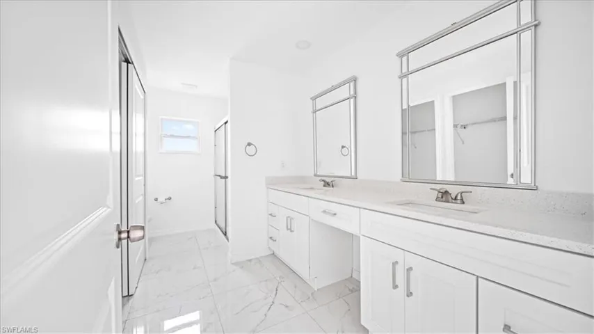 Full bath featuring double vanity, a shower stall, and light marble finish floors
